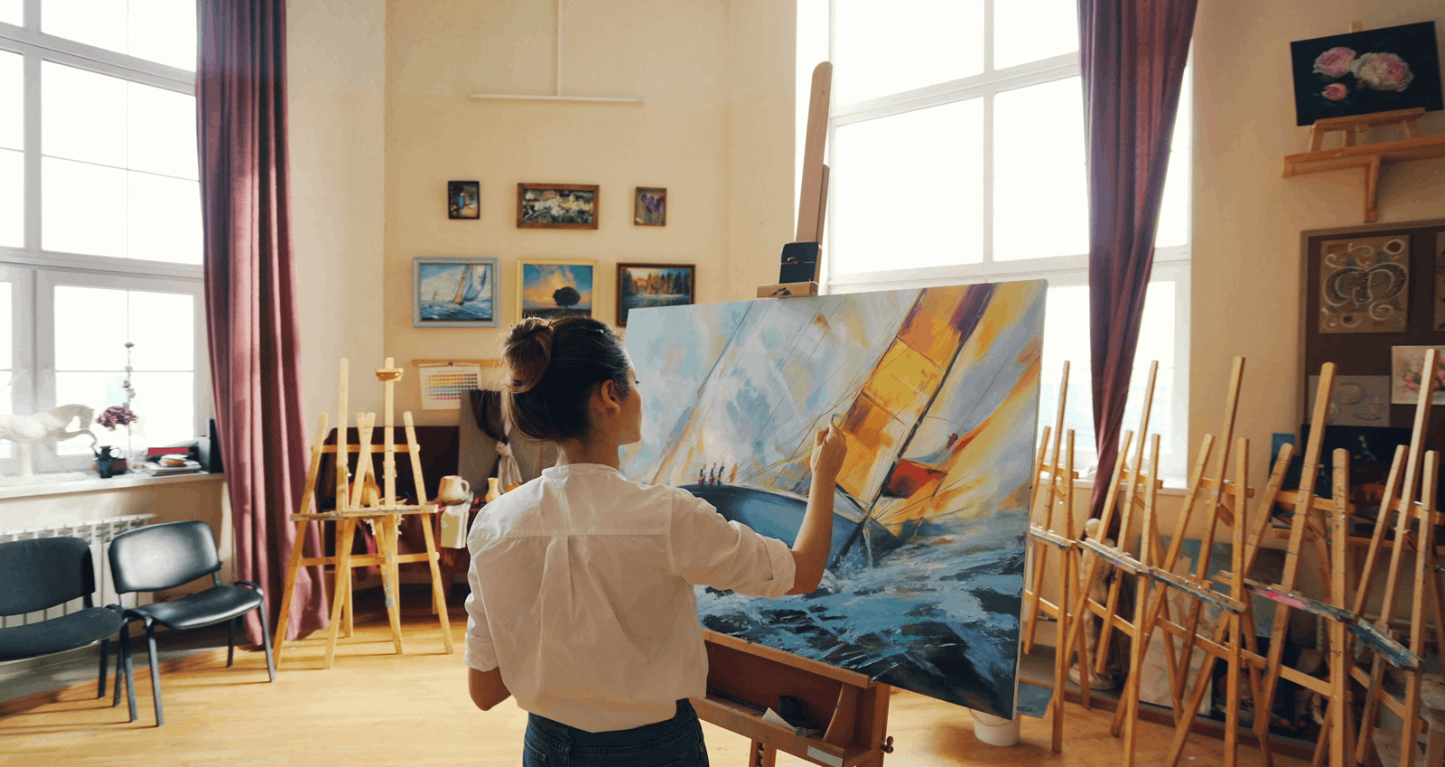 A woman painting a large colourful canvas at an easel during a private art session in a bright studio.