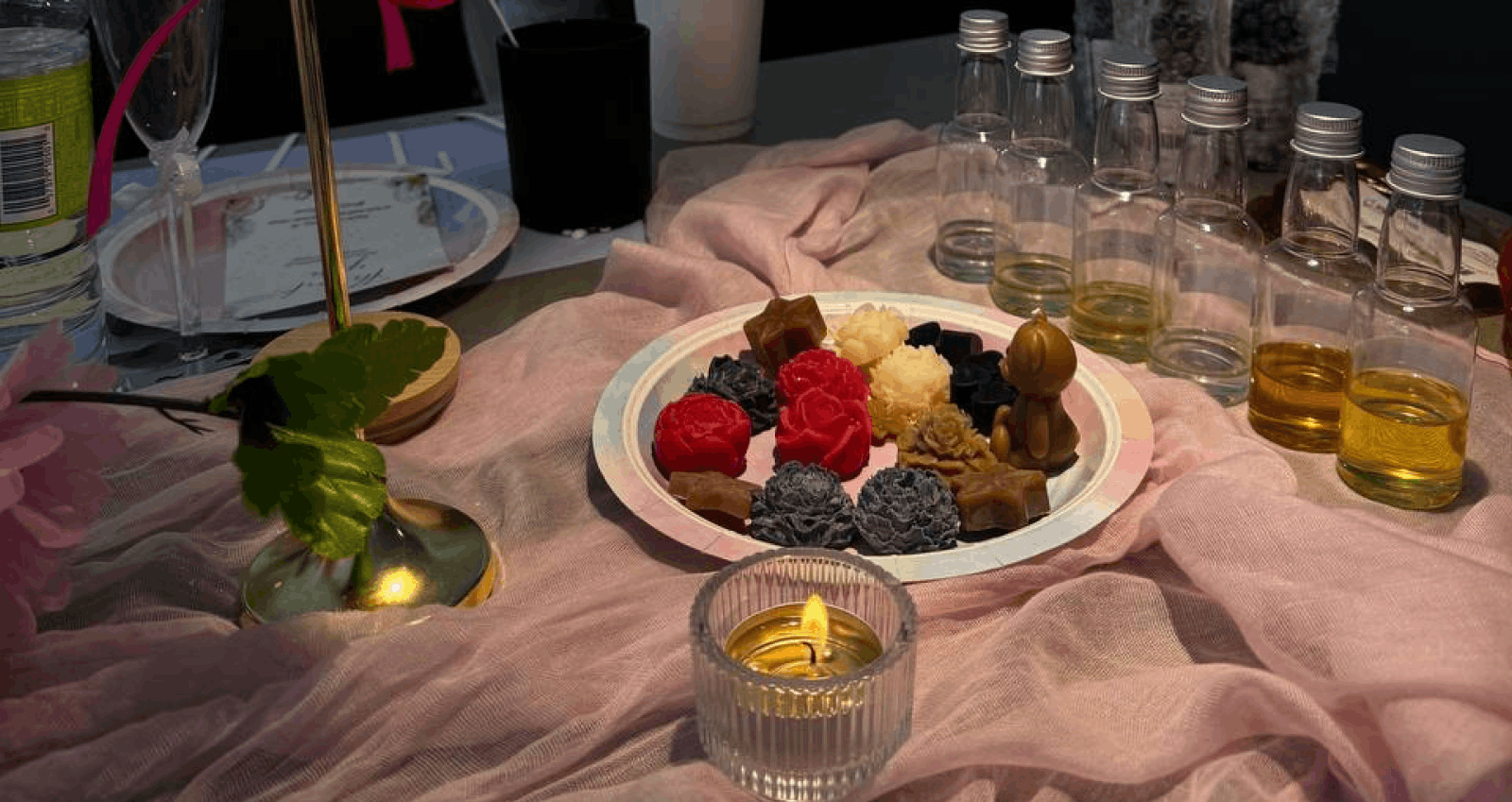 A table set for a candle making workshop in Calgary — scented wax shapes, dried botanicals, and a lit candle in a glass holder.